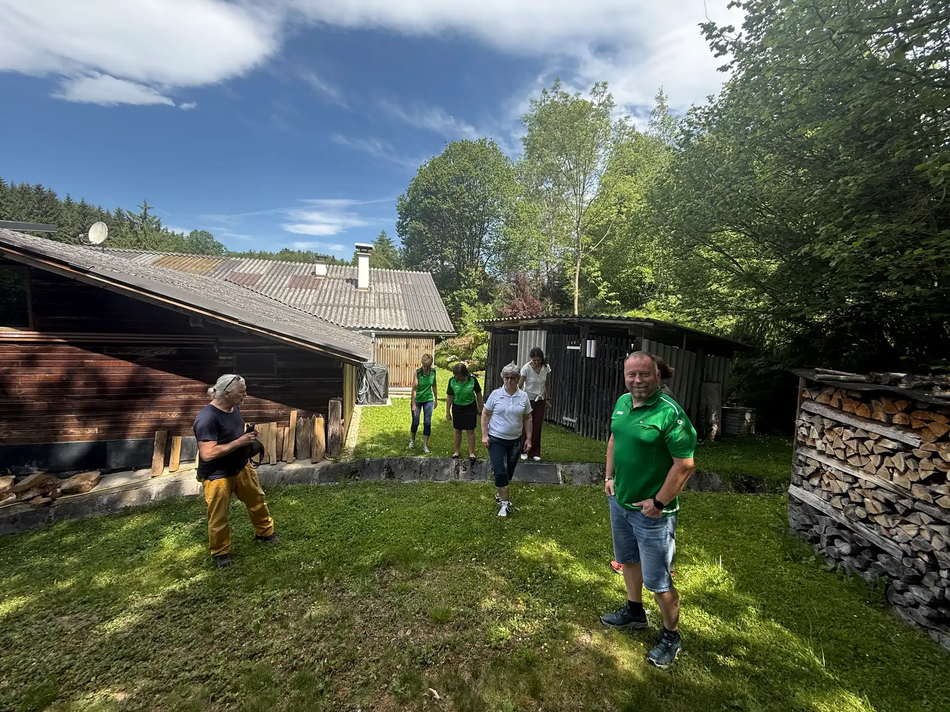 Auch das Gelände wurde unter die Lupe genommen. Mehrere Personen in grünen Naturfreunde-Shirts bewegen sich über ein Wiesengelände mit Holzhütten und Bäumen im Hintergrund.